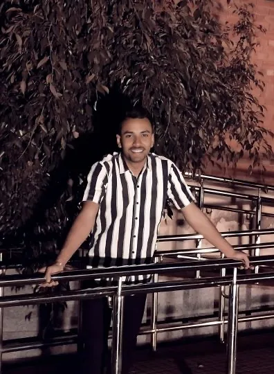 Anit Jha smiling, leaning on a steel railing under a tree at night